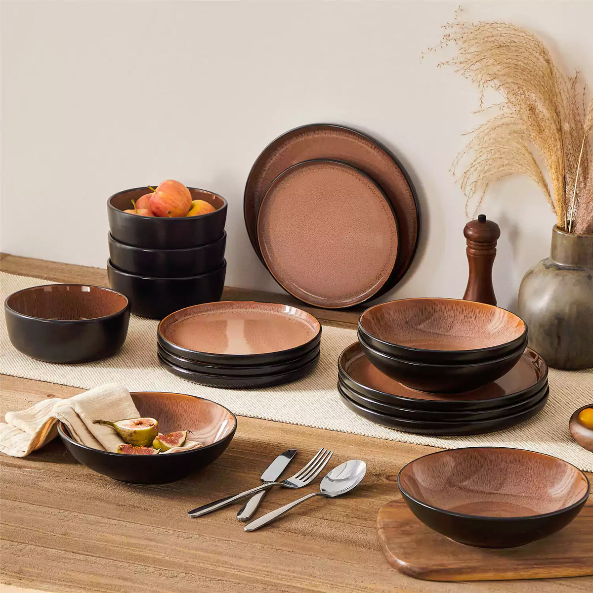 Amber red stoneware dinnerware set with a fig-topped soup plate on a brown wooden table and beige table runner.