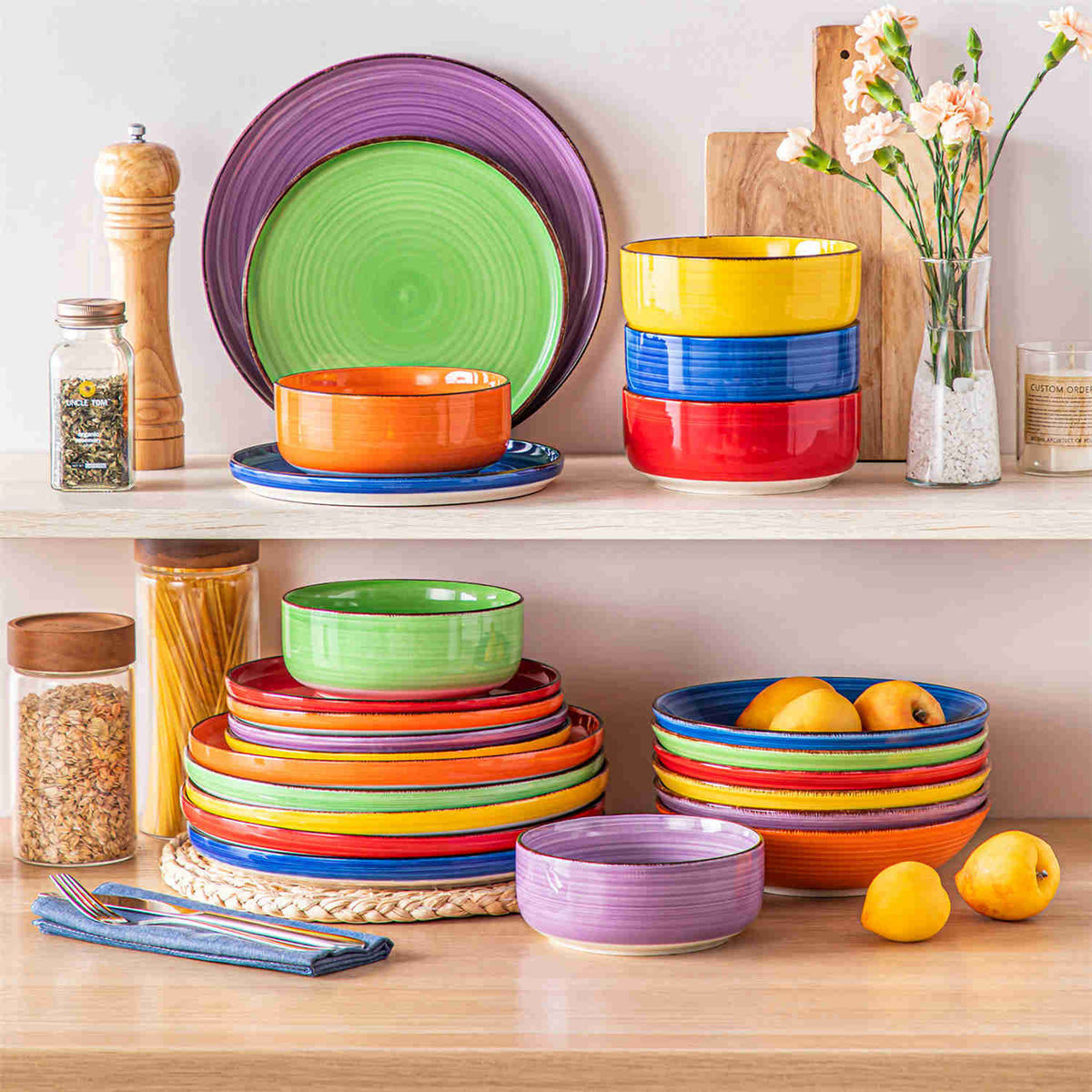 Colorful 24-piece Bonita lipped-edge stoneware dinnerware set stacked on wooden cabinet with flowers, fruit, and decorative accents.