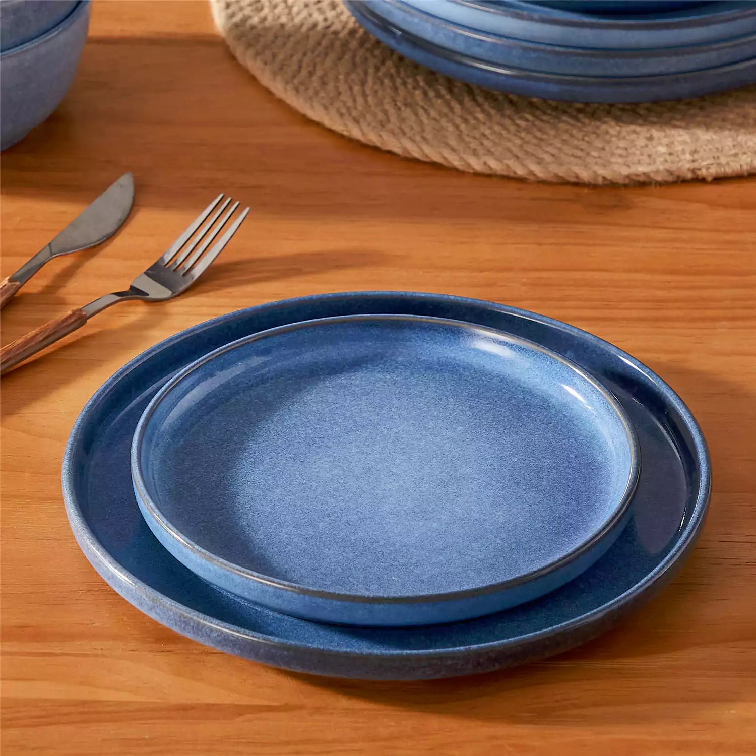 Blue stoneware plates and bowls with reactive glaze on farmhouse wooden table with woven placemats