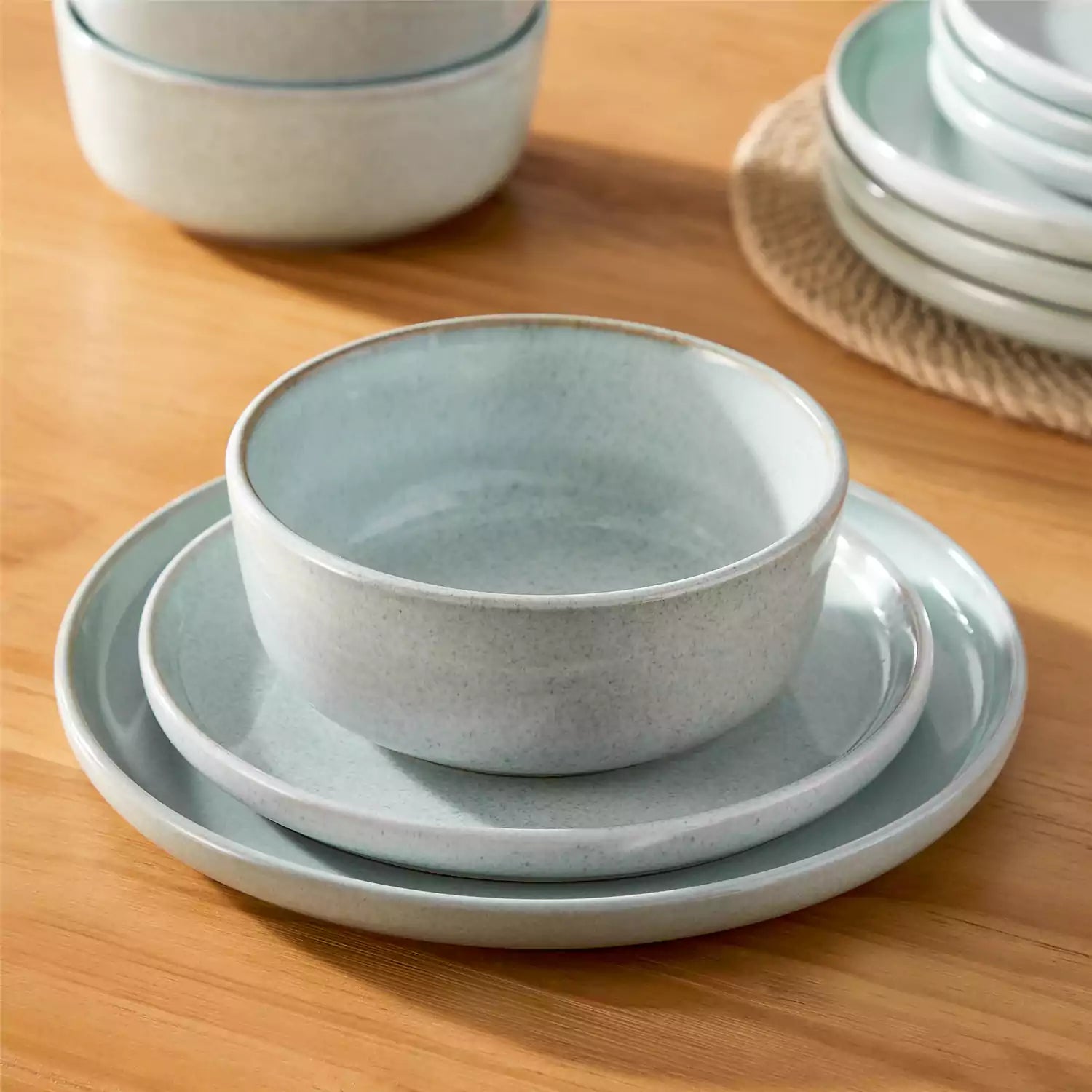 Mint green stoneware plates and bowls with reactive glaze on farmhouse wooden table with woven placemats