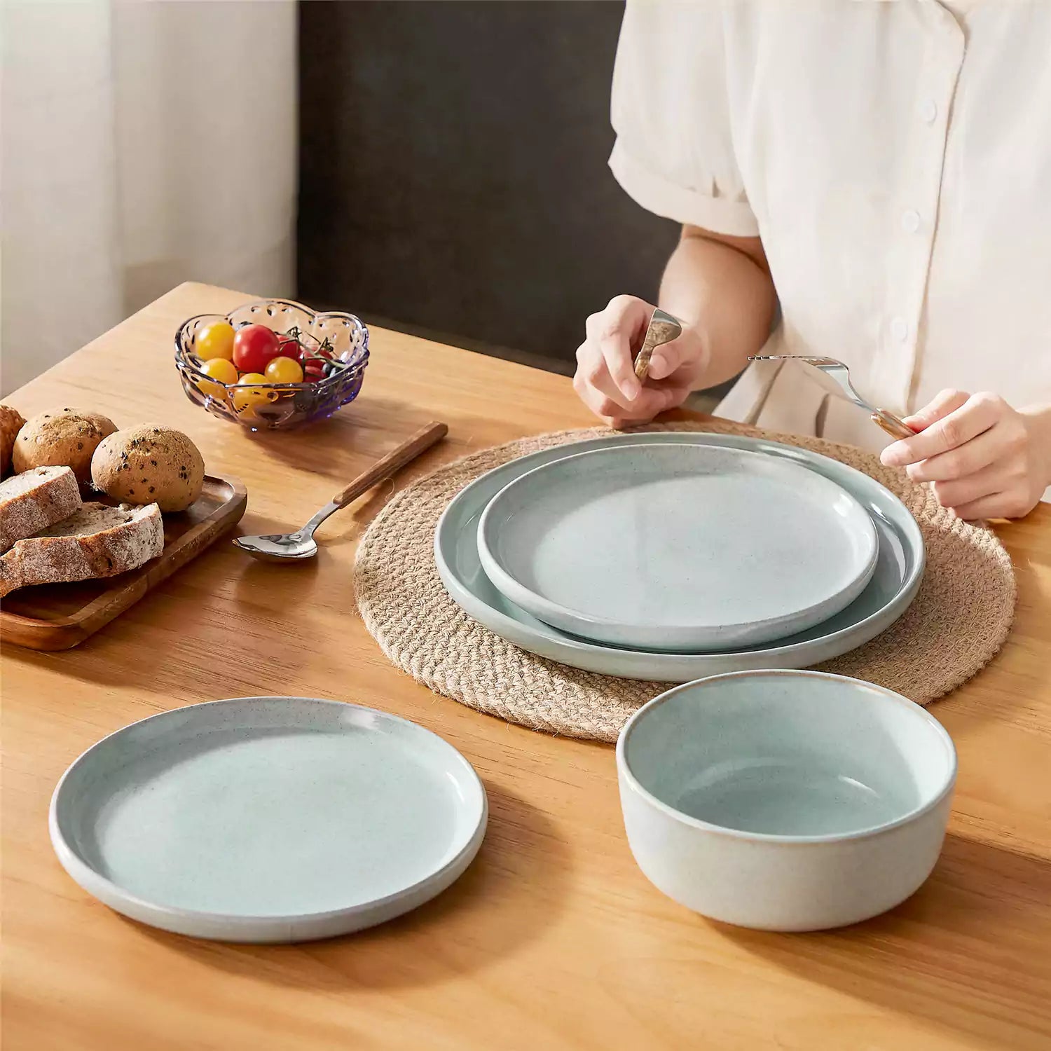 Mint green stoneware plates and bowls with reactive glaze on farmhouse wooden table with woven placemats
