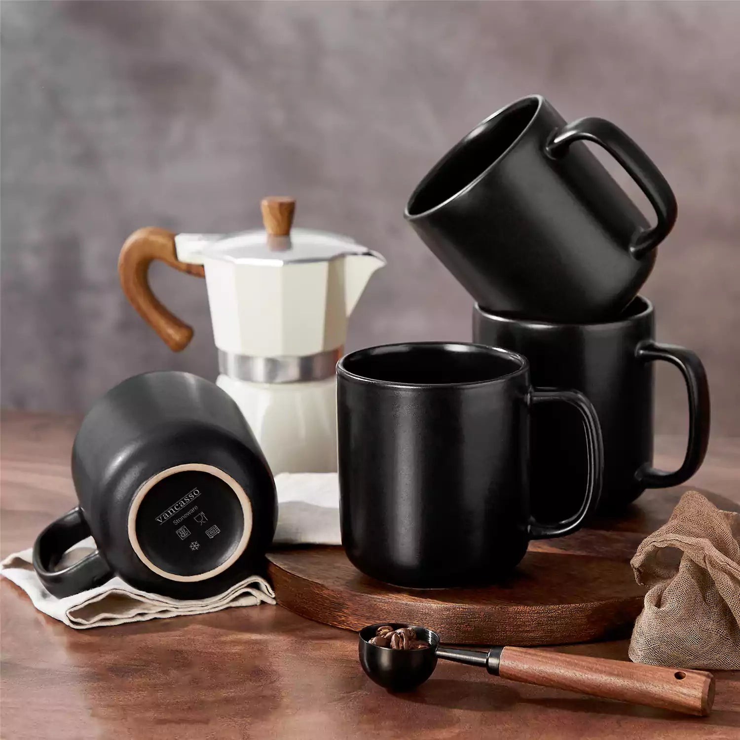 Playa 16oz stoneware mugs in black reactive glaze on a rustic wooden café table with coffee maker and pastries
