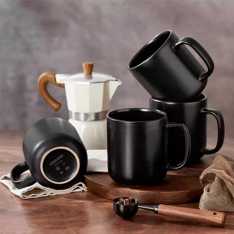 Playa 16oz stoneware mugs in black reactive glaze on a rustic wooden café table with coffee maker and pastries