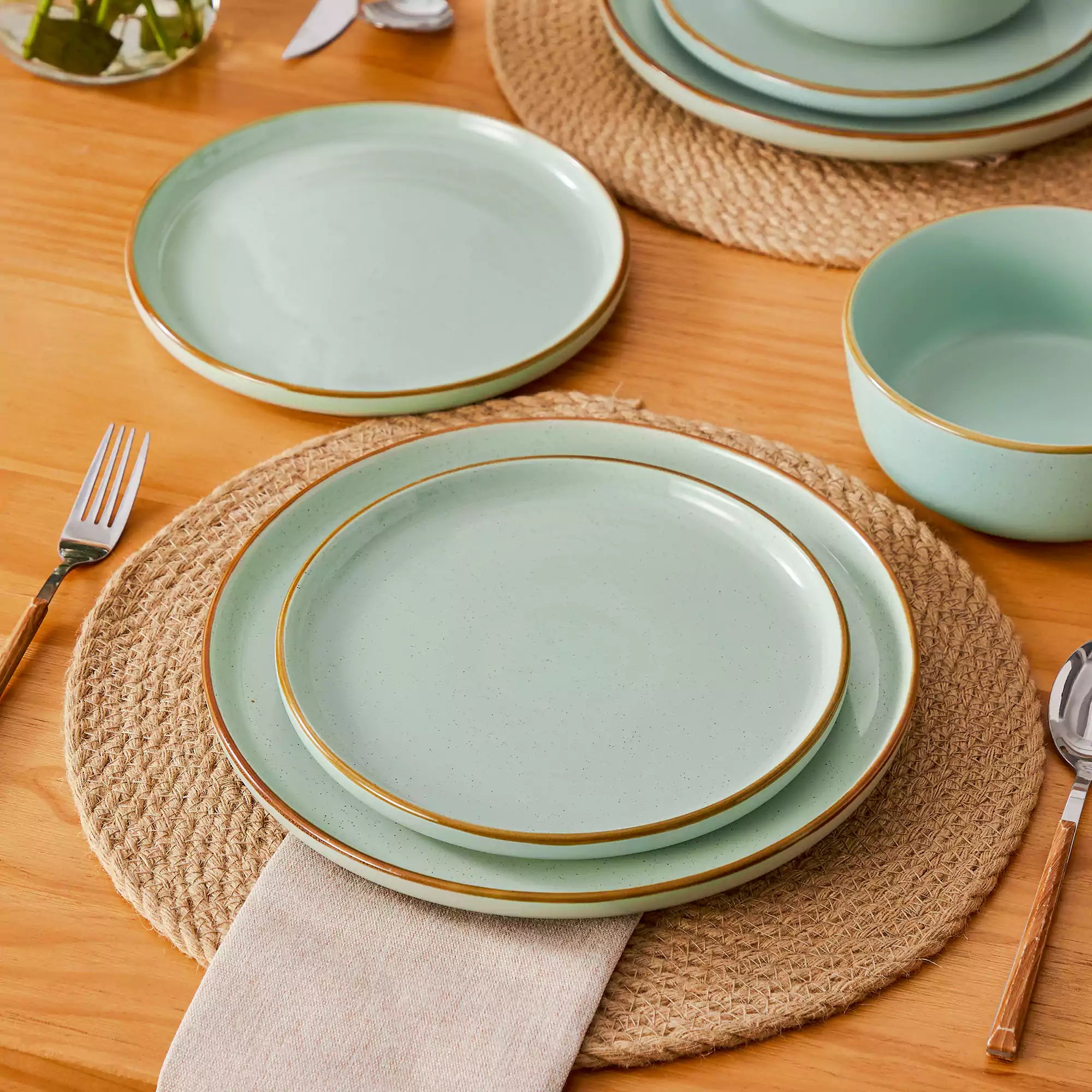 Green rustic stoneware dinnerware set with speckled - lipped-edge plates and bowls on a dining table with flowers and cutlery in a cozy modern kitchen-vancasso