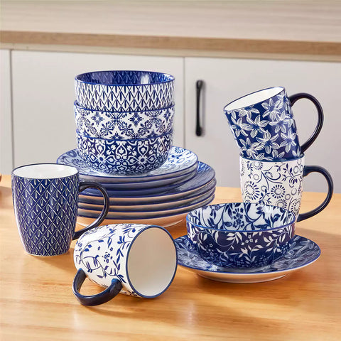 Selene 16-piece porcelain set in indigo patterns - showcasing plates - bowls - and mugs beautifully styled with vibrant meals on a rustic wooden table