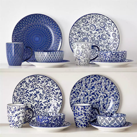 Selene 16-piece porcelain set in indigo patterns - showcasing plates - bowls - and mugs beautifully styled with vibrant meals on a rustic wooden table