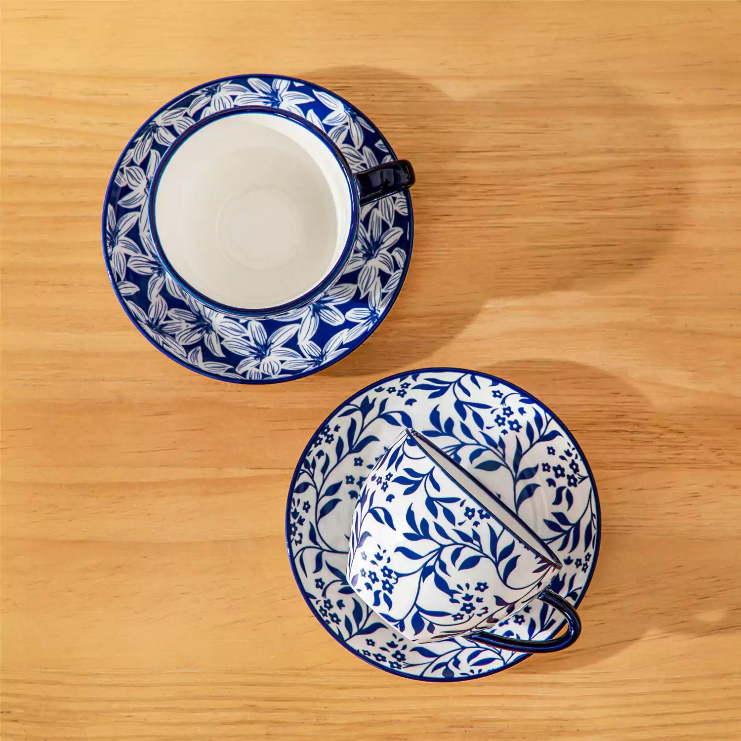 Set of 4 Selene indigo floral porcelain cups and saucers on a wooden table with coffee and pastries featuring blue and white Japanese style mix and match patterns