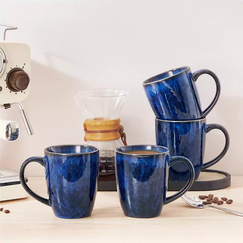 Set of 4 Starry 16oz stoneware mugs in blue with reactive glaze finish styled on a marble countertop with fresh coffee