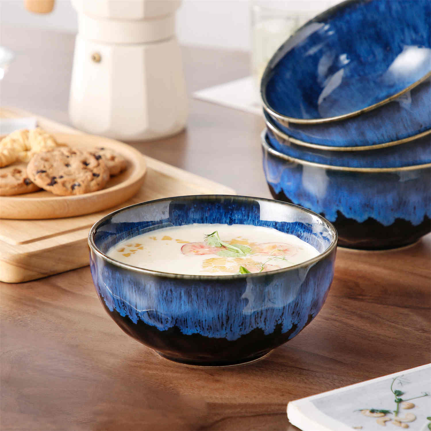 Starry reactive glaze cereal bowls in blue on a rustic wooden table - filled with creamy soup - pasta - and fresh fruit salad for a cozy - celestial dining vibe