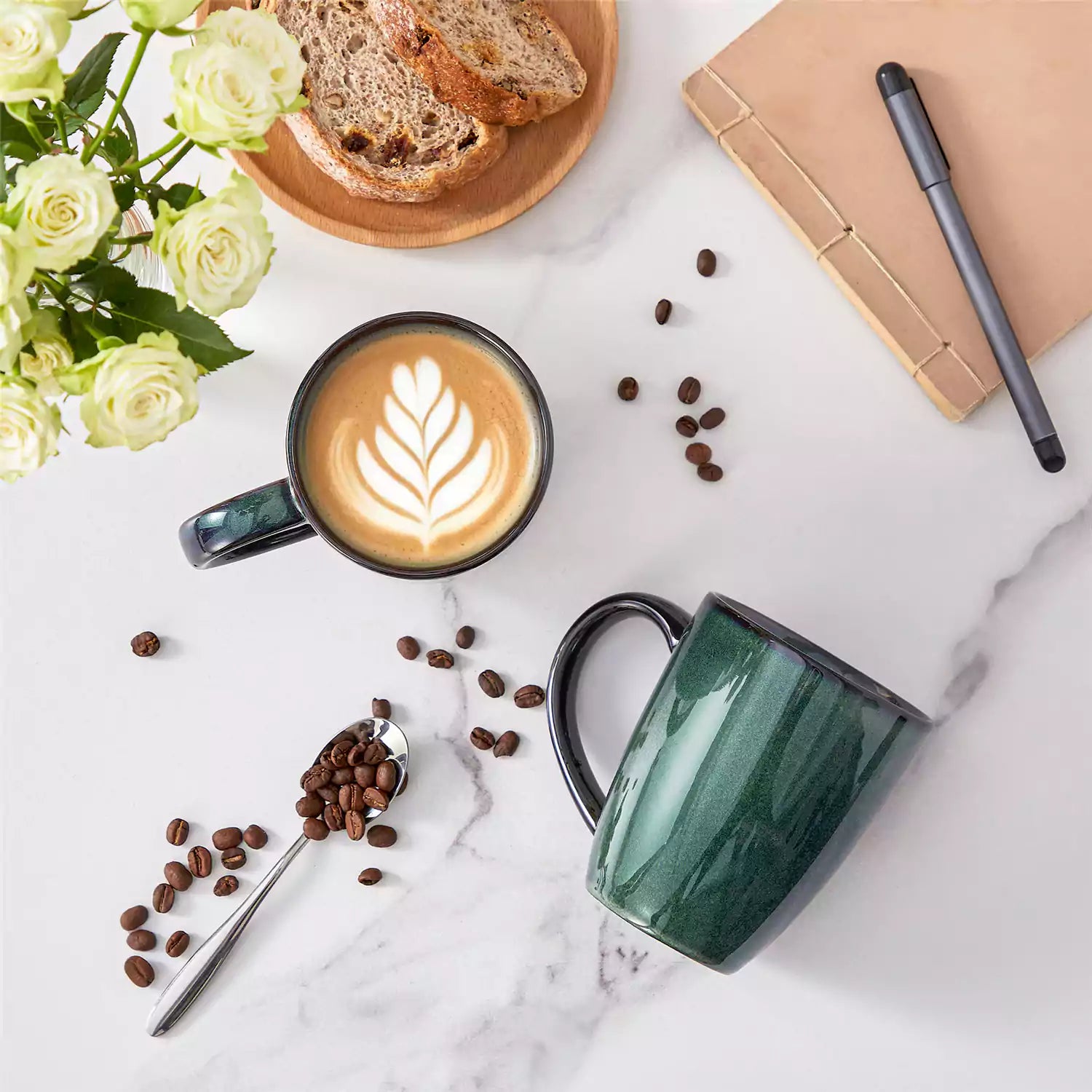 Set of 4 Starry 16oz stoneware mugs in green with reactive glaze finish styled on a marble countertop with fresh coffee