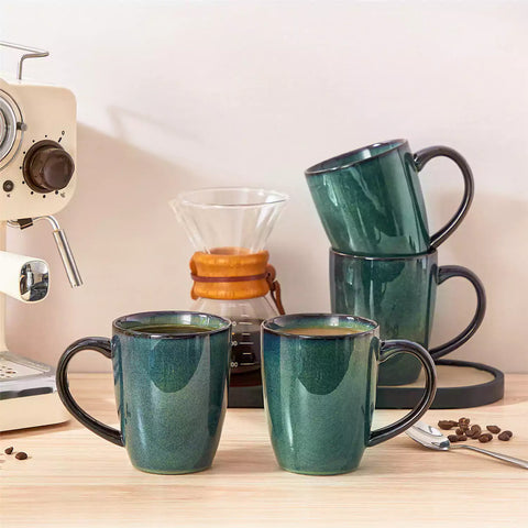 Set of 4 Starry 16oz stoneware mugs in green with reactive glaze finish styled on a marble countertop with fresh coffee