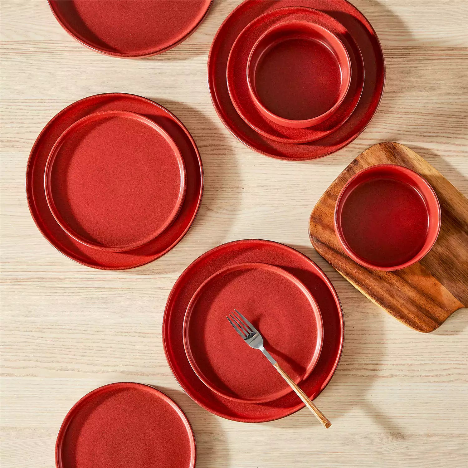 Red reactive glaze stoneware dinner plates styled with food on rustic wood table with woven placemats modern minimalist tableware set